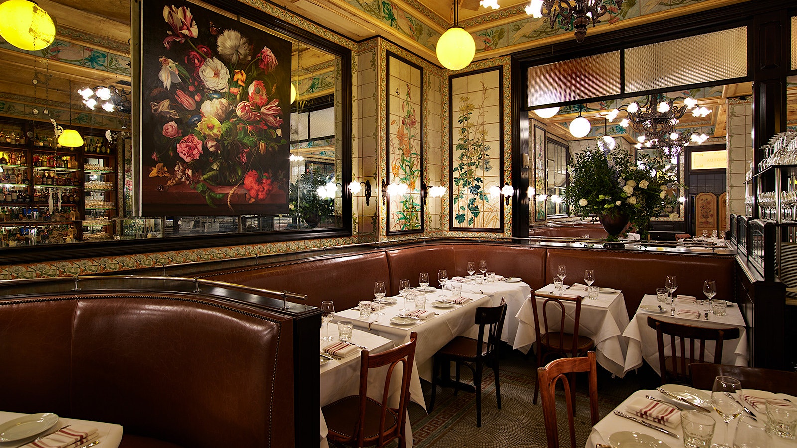  Comedor estilo bistró Le Gratin con bancos, sillas de madera, paredes cubiertas con espejos y azulejos de colores, y un cuadro floral del artista Marc Dennis